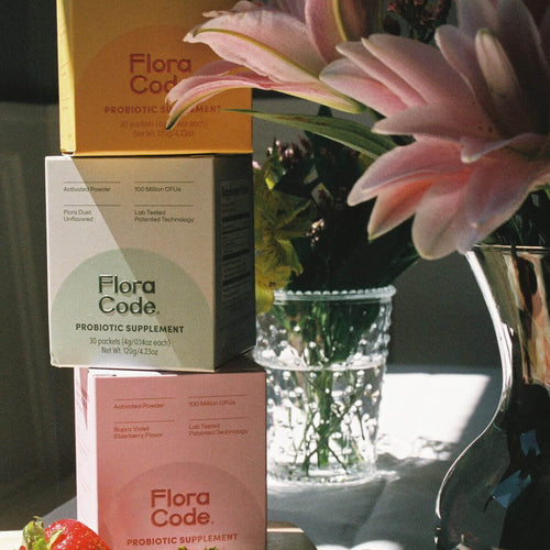 stack of flora code probiotics next to flowers